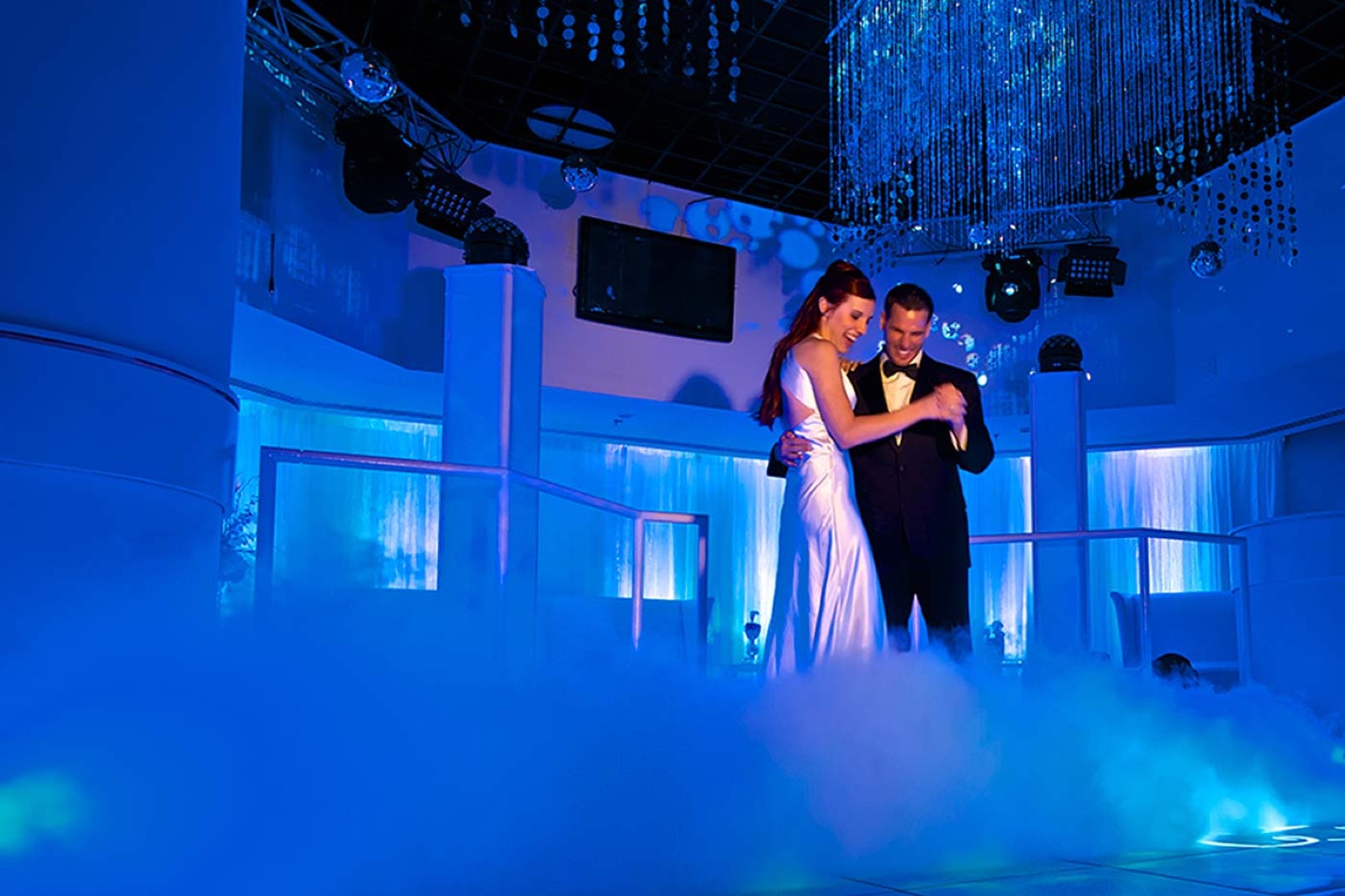 A couple dancing on a low cloud of fog under blue light