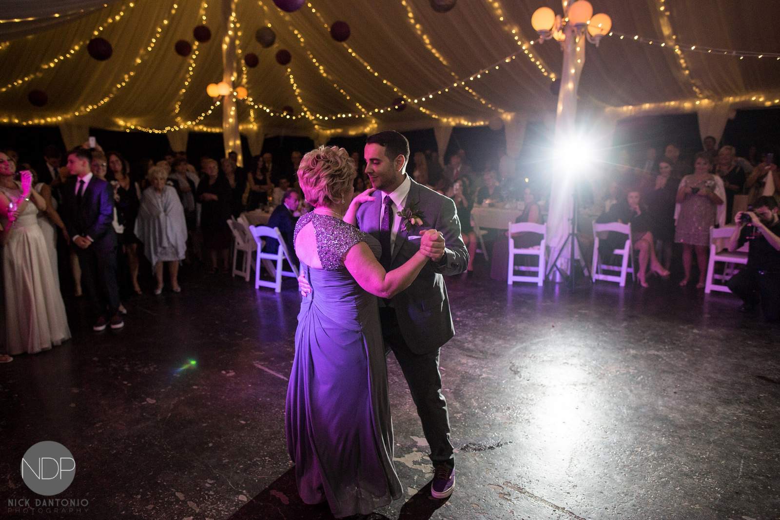 A groom dances with his mother under string lights